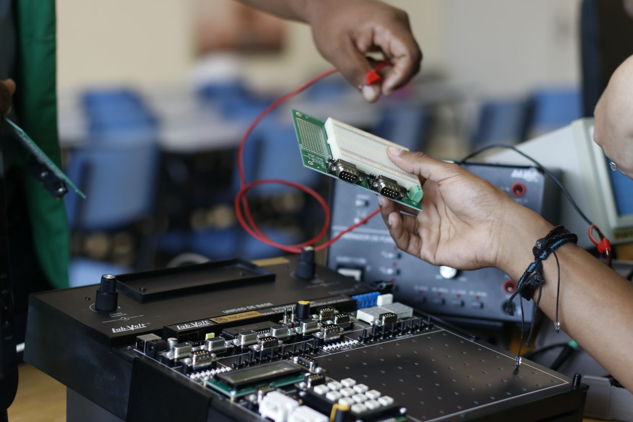 Services Close-up of hands working with electronics equipment and circuit board in a lab setting.