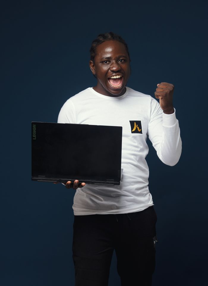 Services Confident man in white shirt celebrates success while holding a laptop against blue background.
