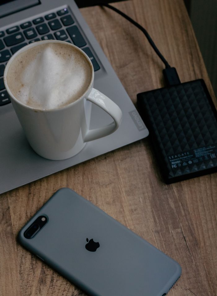 About Cozy workspace with laptop, phone, coffee, and external hard drive on wooden table.