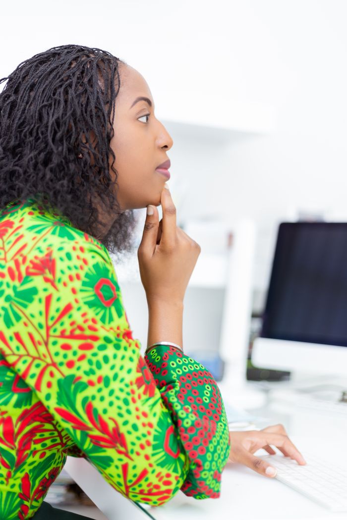 Services African woman in a bright green pattern dress, focused at her desk in an office setting.