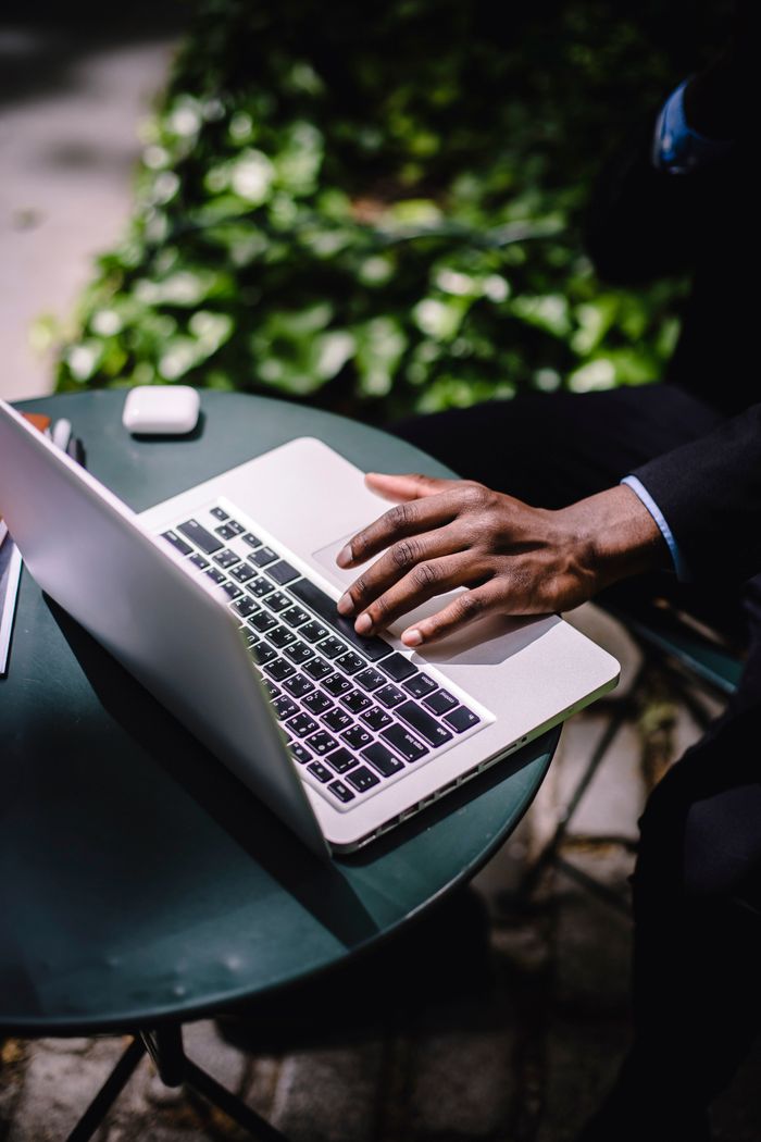 About From above of crop faceless African American businessman browsing netbook while sitting at round table in cozy outdoor cafe